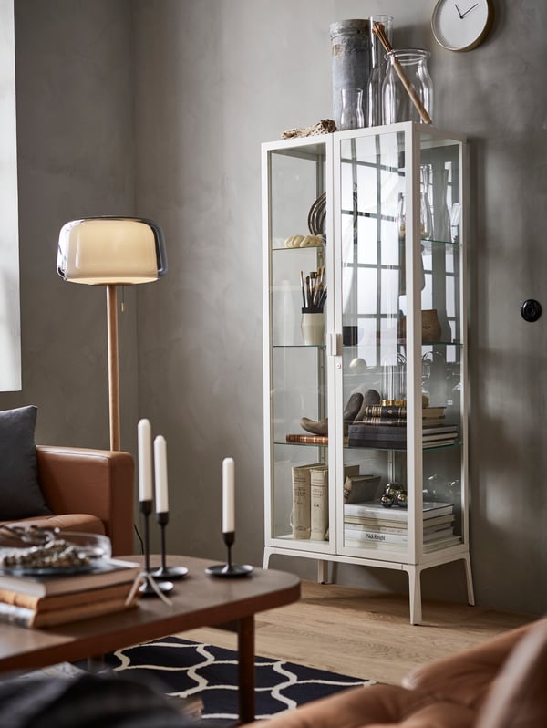 IKEA MILSBO glass cabinet with a white frame, various items on display on the shelves, and a table plus lamp.