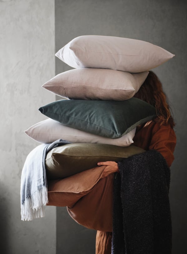 Three cushions with different covers are stacked on top of each other on an ALSEDA stool near a window with a curtain.