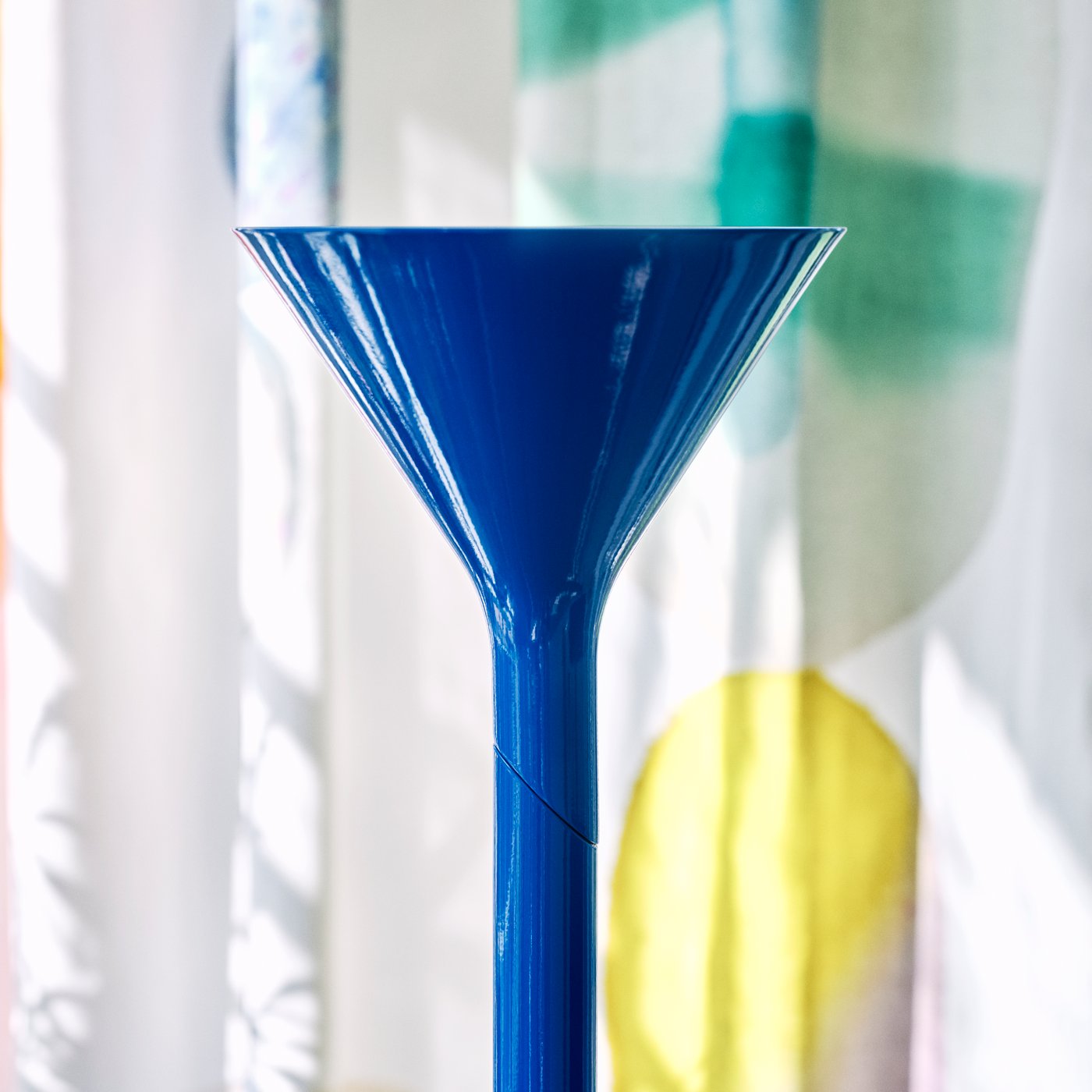 En närbild på en glansig, kungsblå lampa med en distinkt trattform, placerad mot en färgstark, abstrakt bakgrund.