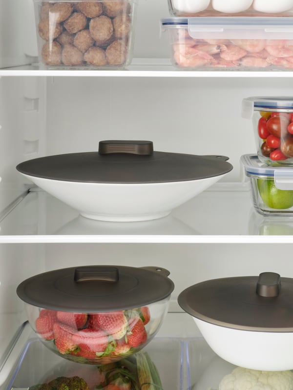 Tapa para contenedores de comida KLOCKREN dentro del refrigerador sobre platos blancos.