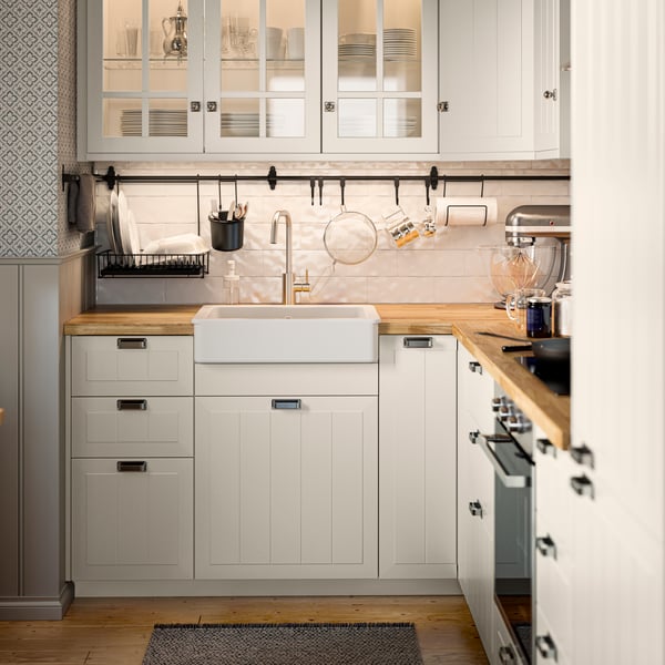 A small, L-shaped METOD kitchen in traditional style with beige, panelled fronts and glass doors.