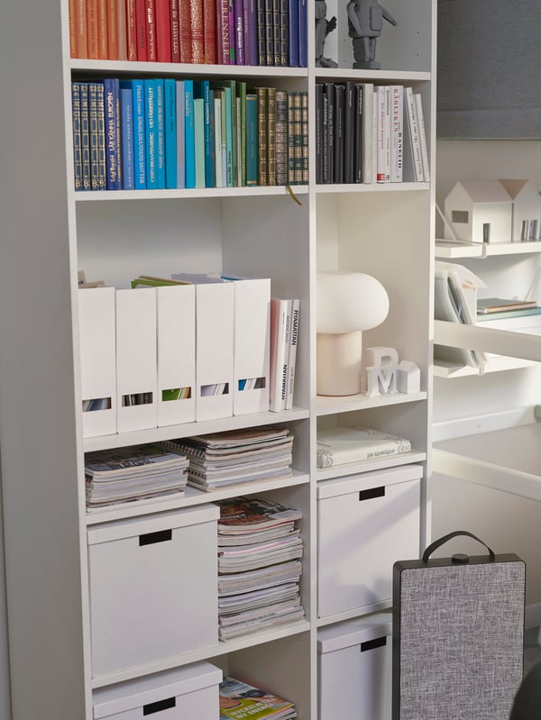 A VIHALS shelving unit is filled with books, magazine boxes, storage boxes and lamp. An air purifier sits on the floor.