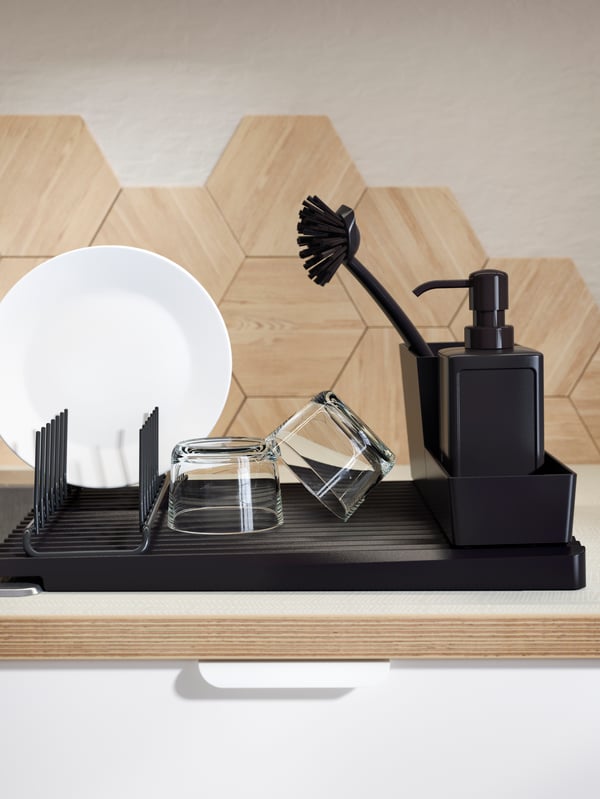 A RINNIG multi-functional dish rack made of plastic covered steel on a draining board with plates, bowls and a glass.