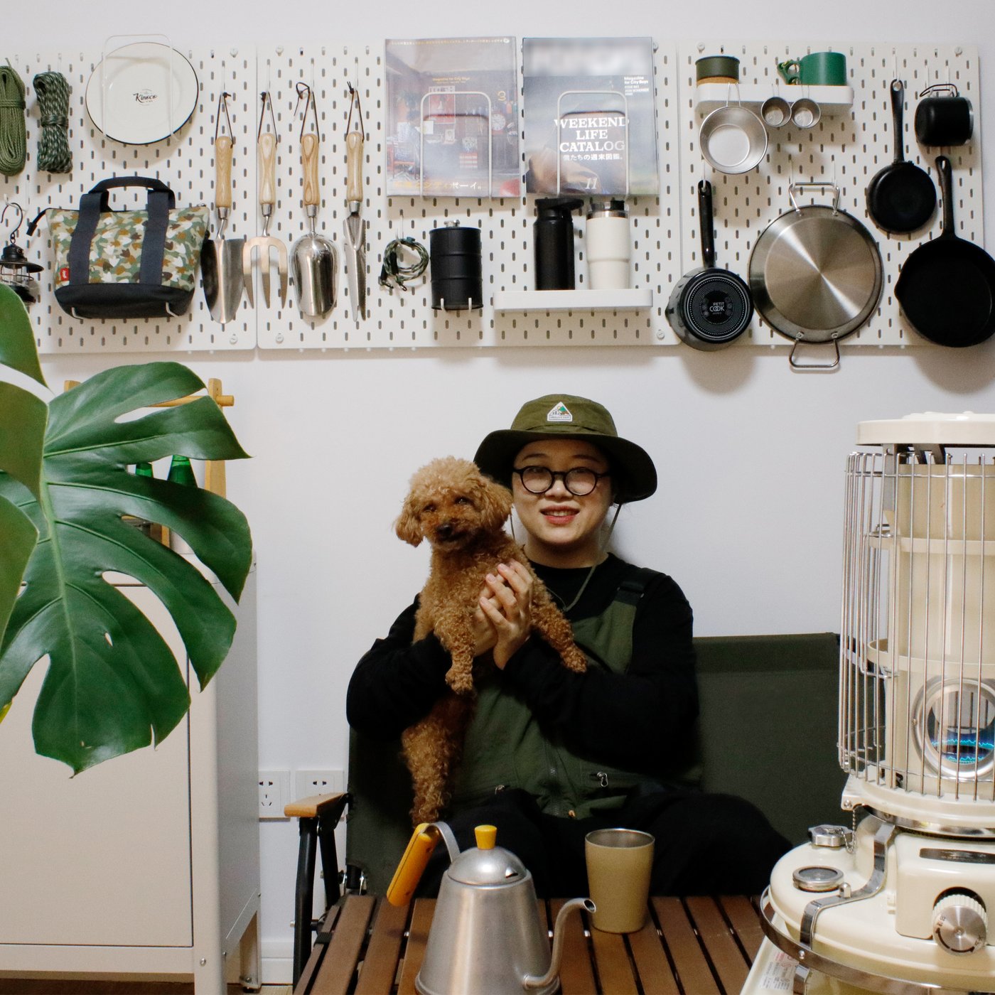 Doris and her pet dog posing with her camping gear that’s stacked up on a wall.