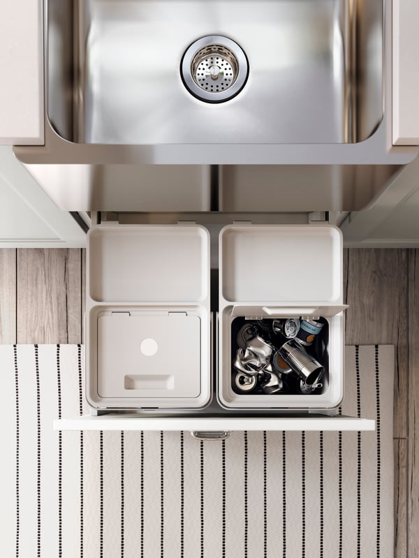 A kitchen drawer is open and light grey HÅLLBAR bins with lids are inside. Aluminium cans are sorted in one of the bins.