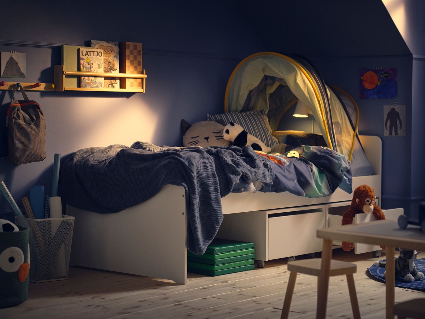 Le coin d’une chambre d’enfant avec un mur bleu dans la lumière du soir, un lit SLÄKT avec du linge de lit bleu et une tente pour lit.