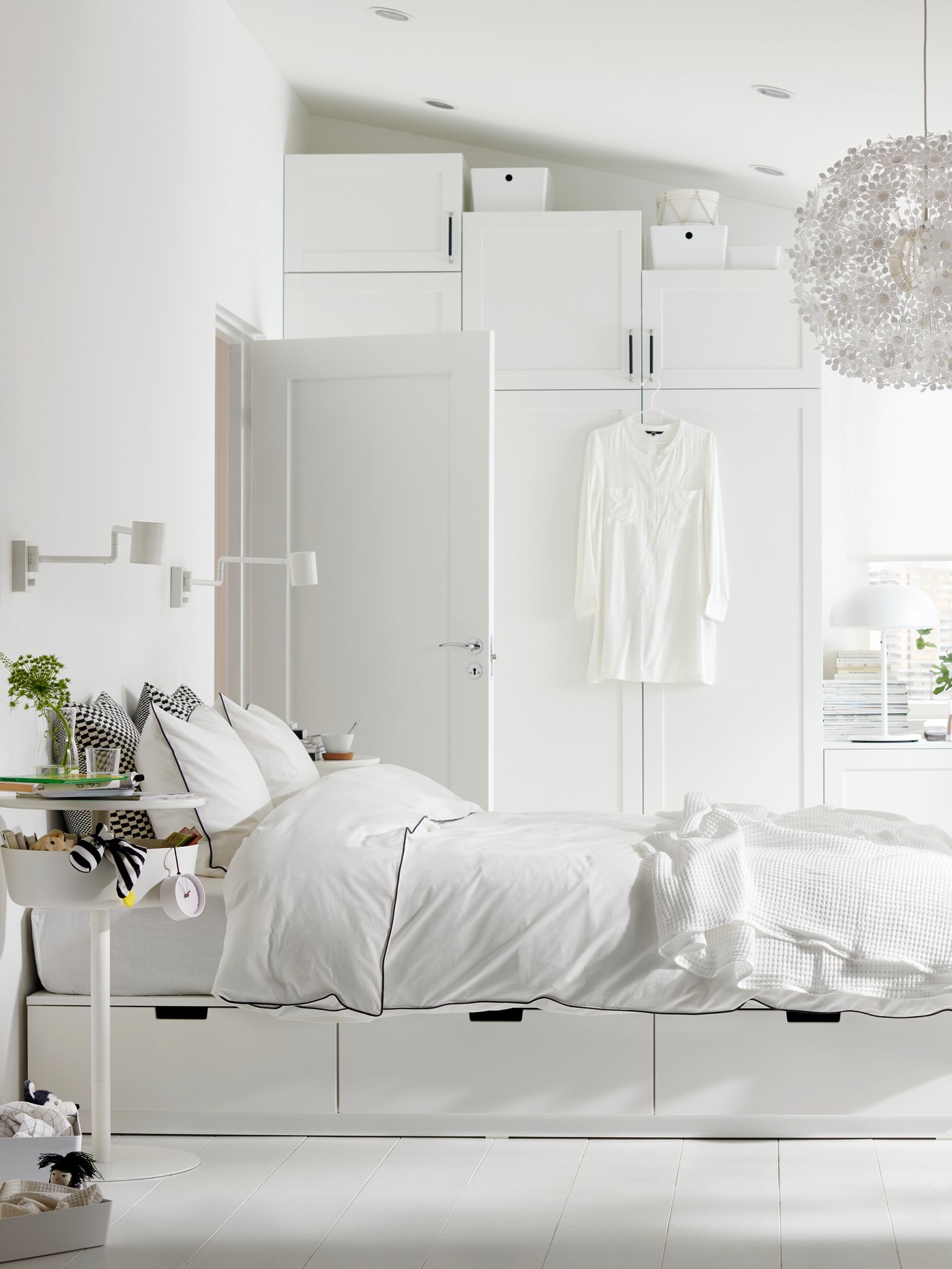 A bright, white bedroom with a NORDLI bed with storage with KUNGSBLOMMA bed linen and a lot of other white furniture.