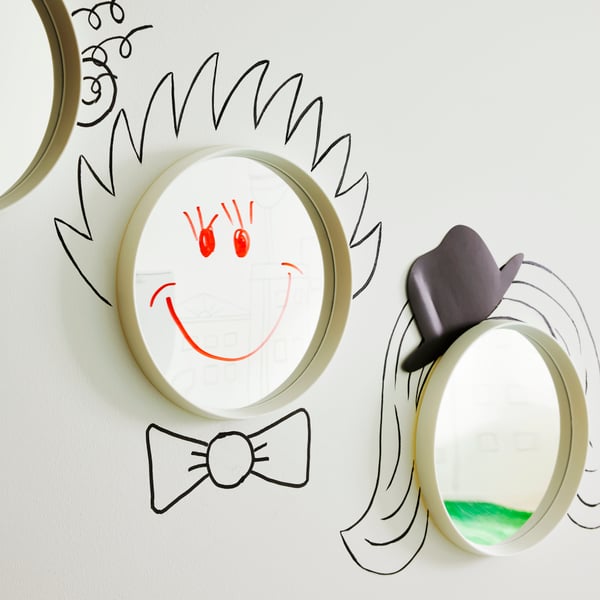 Round white HÄNGIG mirrors on the wall, with hairstyles, hats and smiles drawn on and around them.