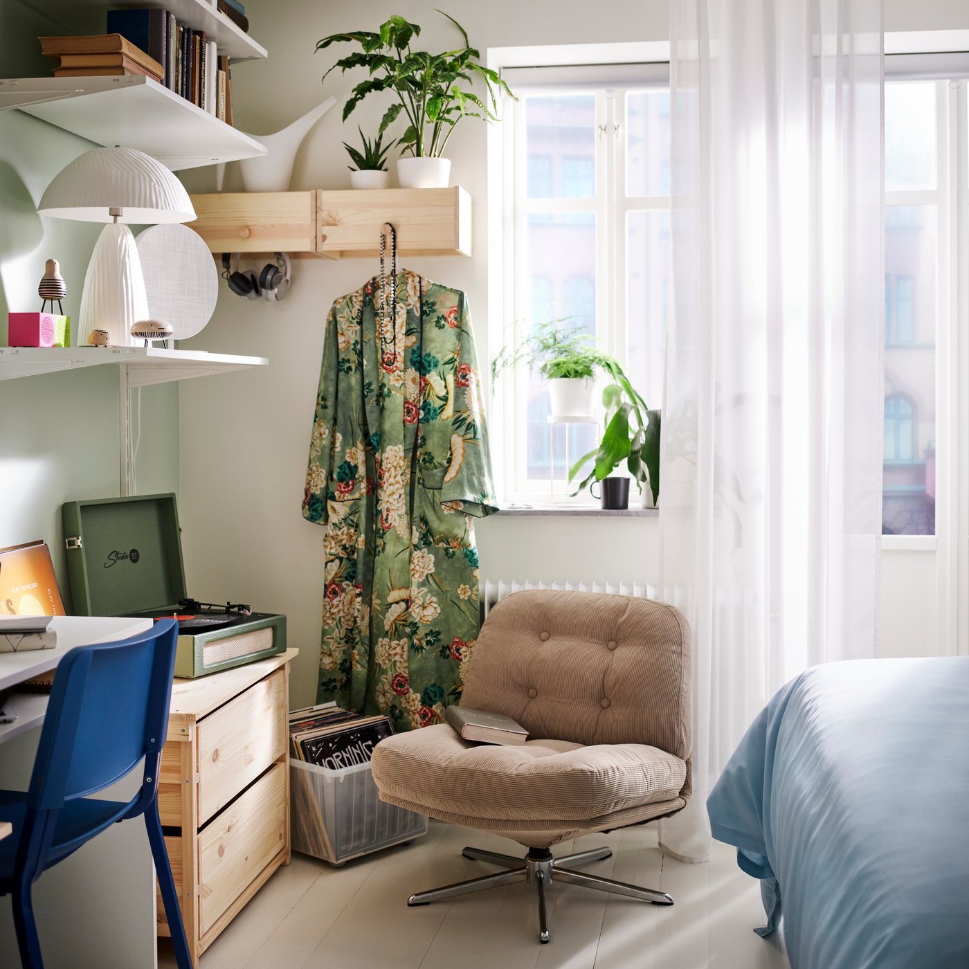A compact bedroom corner with a DYVLINGE swivel easy chair next to a KRONÖREN chest of drawers, plants and shelves.