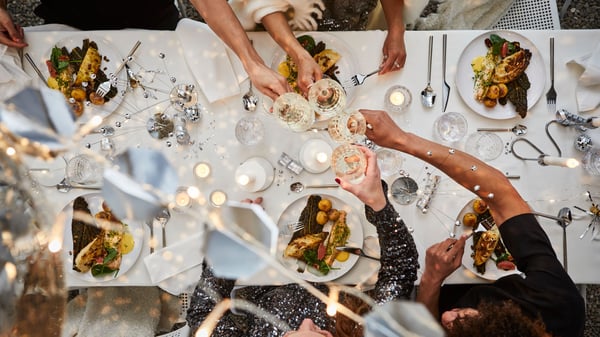 Bird’s-eye view of silver and white New Year’s Eve table setting, raising toast with FRÖJDA champagne coupes.