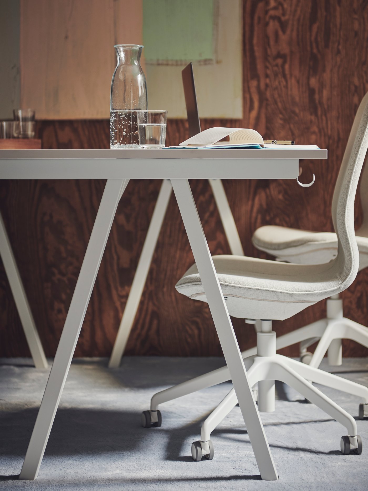 Une chaise de conférence LÅNGFJÄLL GUNNARED beige-blanc glissée sous un bureau réglable.