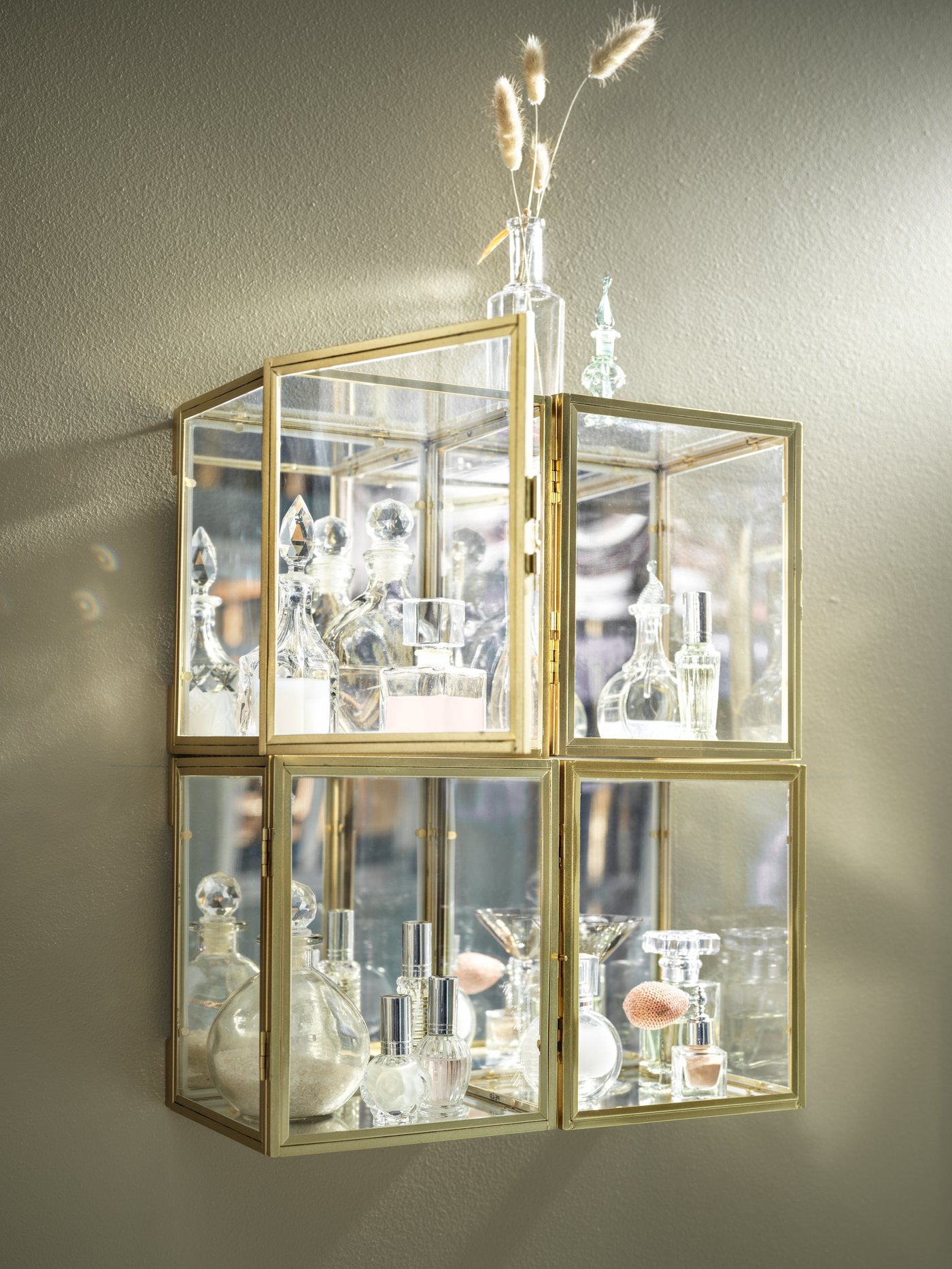 Quatre boîtes vitrées BOMARKEN avec structure dorée réunies et montées au mur, remplies d’une collection de jolis articles en verre.