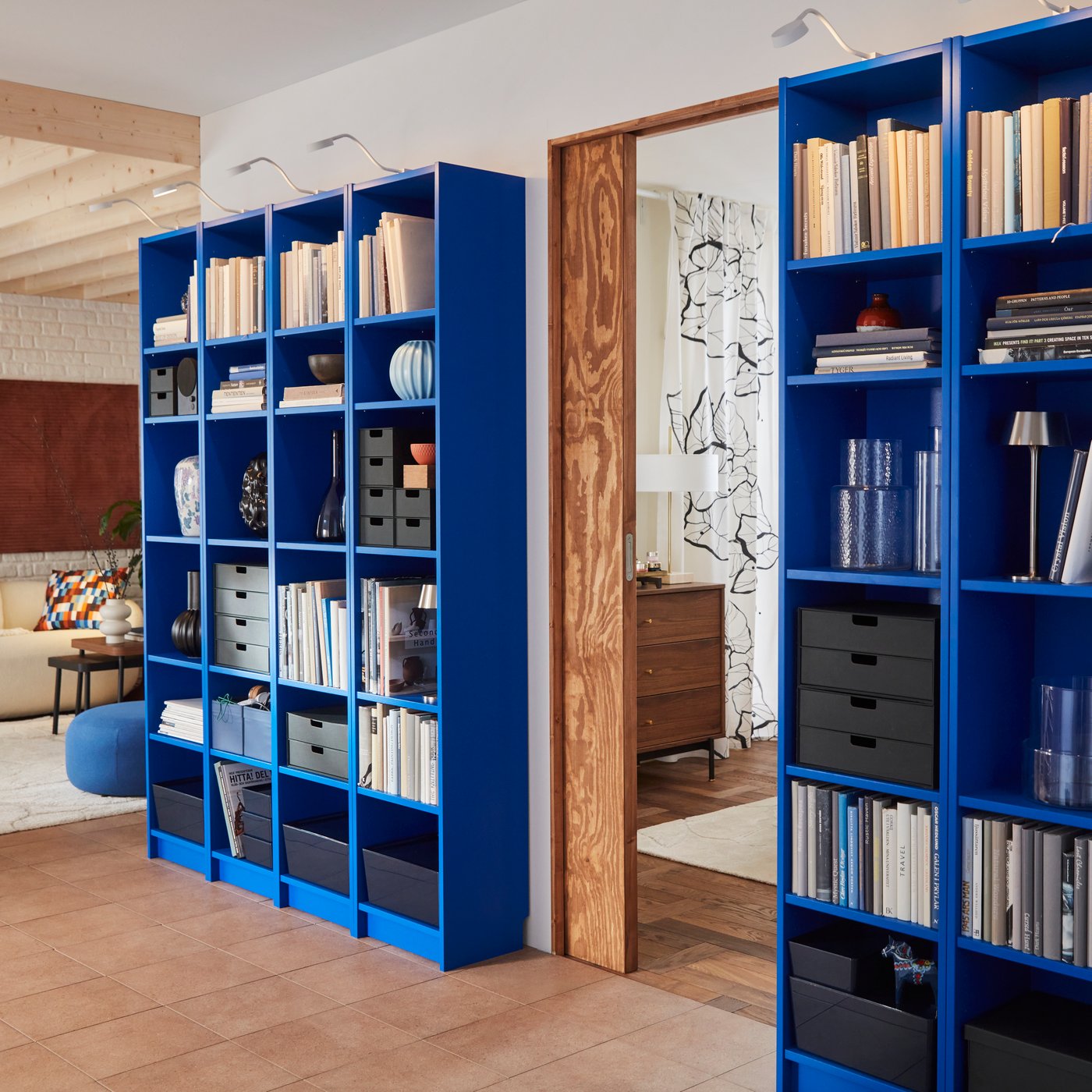 A living room features two blue BILLY bookcases filled with books and decorative items, beside a doorway.