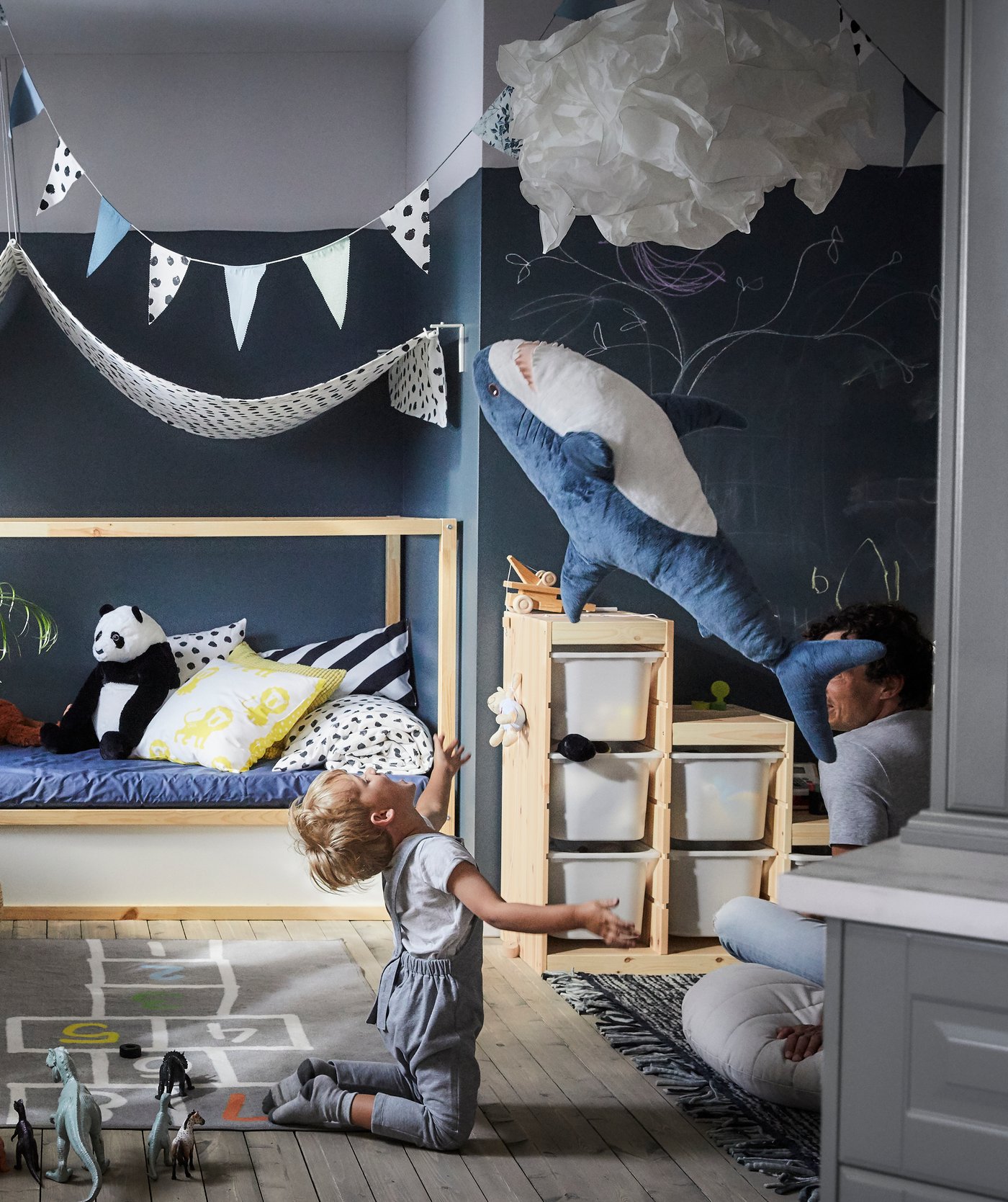 Ein Kind wirft vor dem umbaufähigen KURA Bett in Weiss/Kiefer einen Stofftierhai in die Luft.