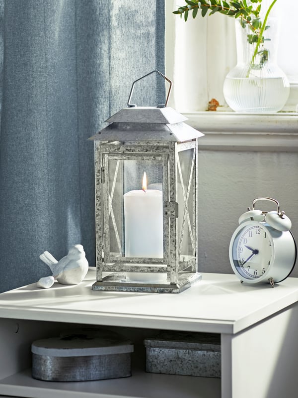 A bright, light space with a BEFÄSTA block-candle lantern and a DEKAD alarm clock placed on a SONGESAND bedside table.