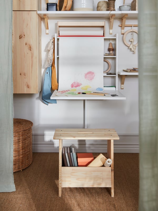A NORBERG wall-mounted drop-leaf tabletop in use. A roll of craft paper above drapes down and shows a kid’s drawing.