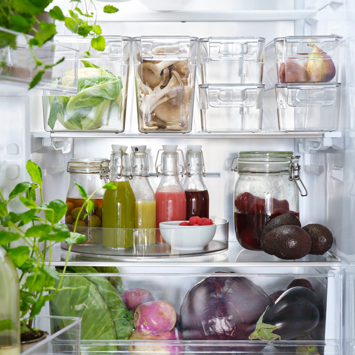 A kitchen fridge containing a transparent KLIPPKAKTUS storage box set of six, holding assorted vegetables and sauces.