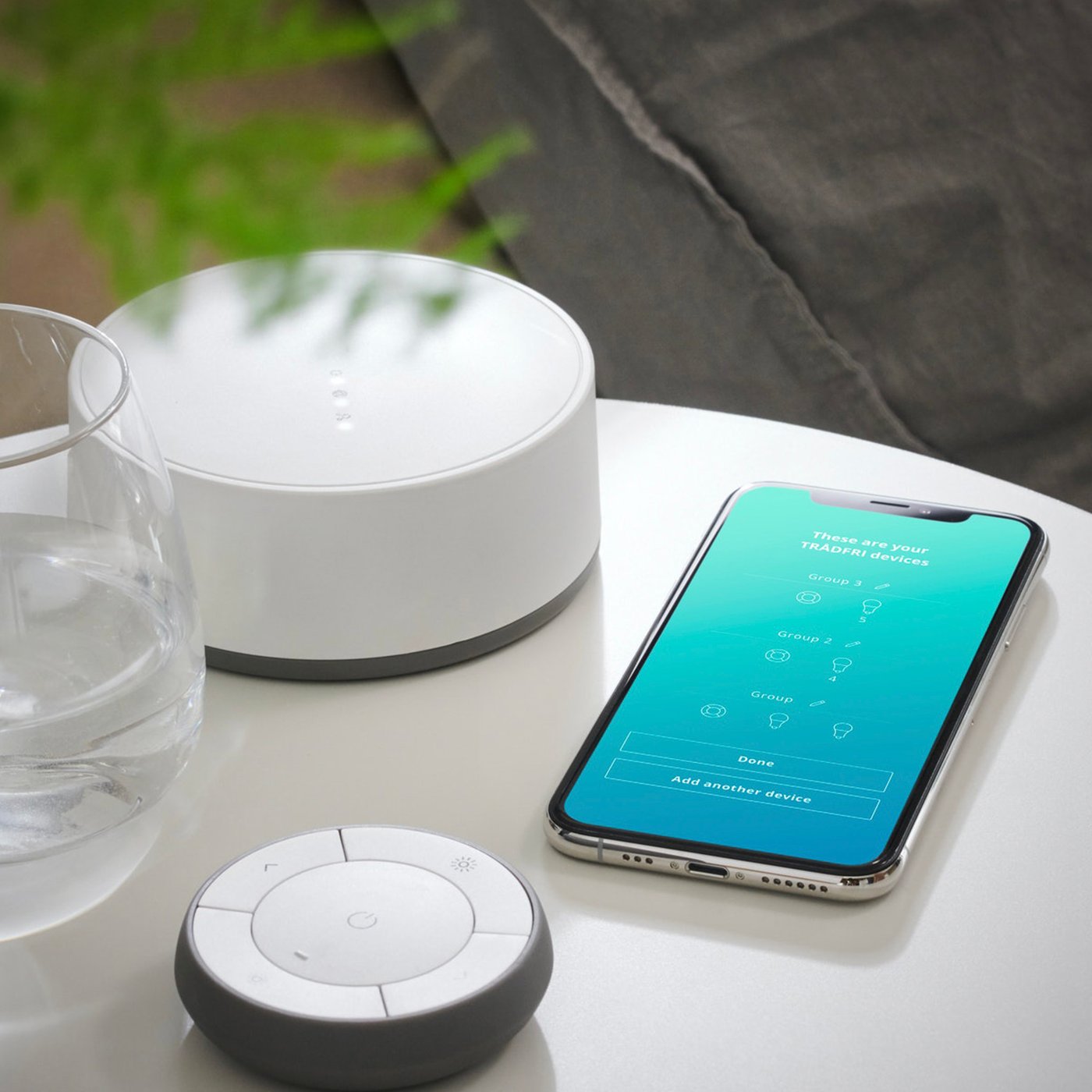 TRÅDFRI mrežni prolaz na noćnom stočiću zajedno s TRÅDFRI daljinskim upravljačem i aplikacijom IKEA Home smart prikazanom na mobilnom uređaju.