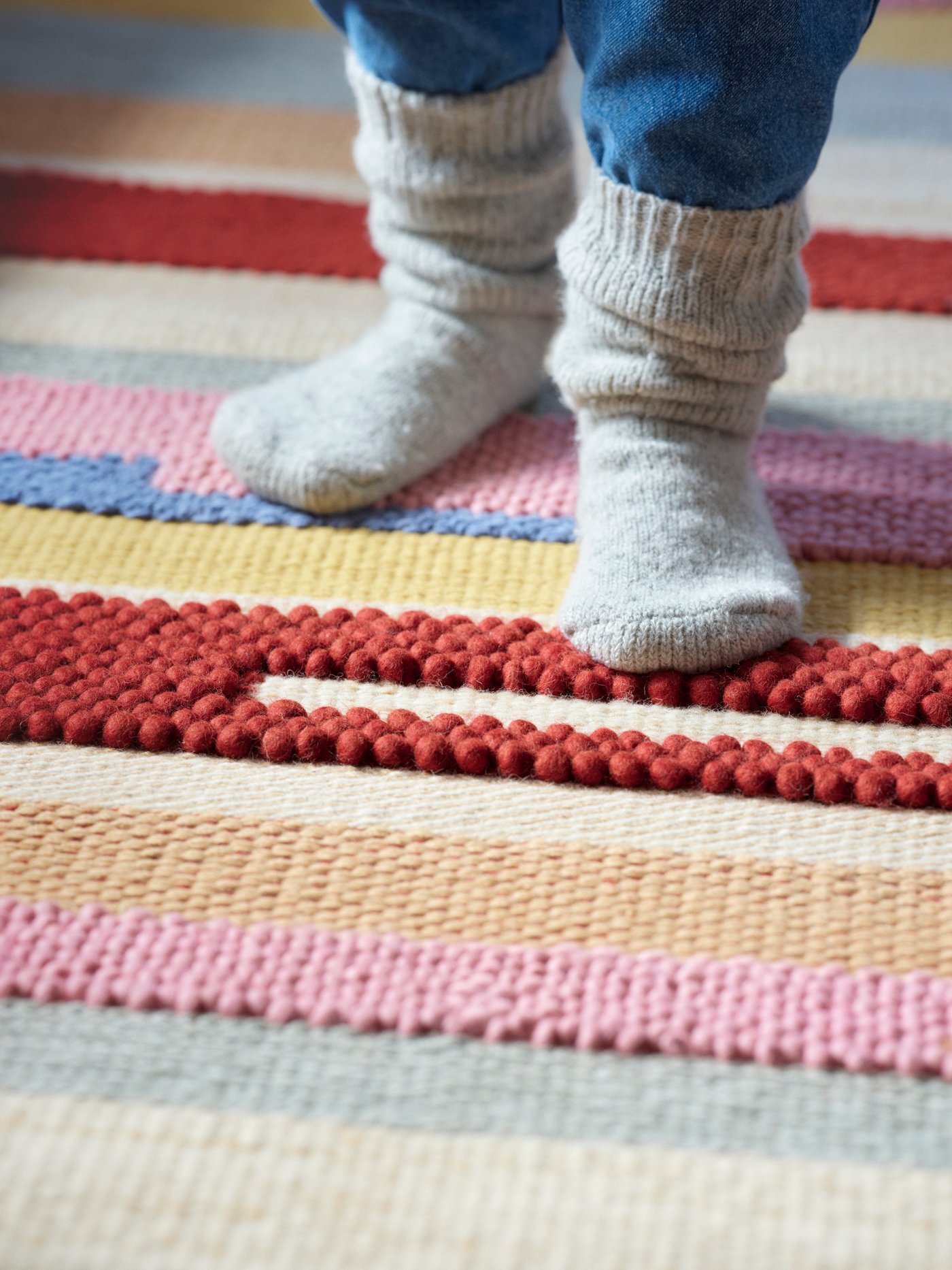 A person wearing wool socks stands on a multi-colored rug.