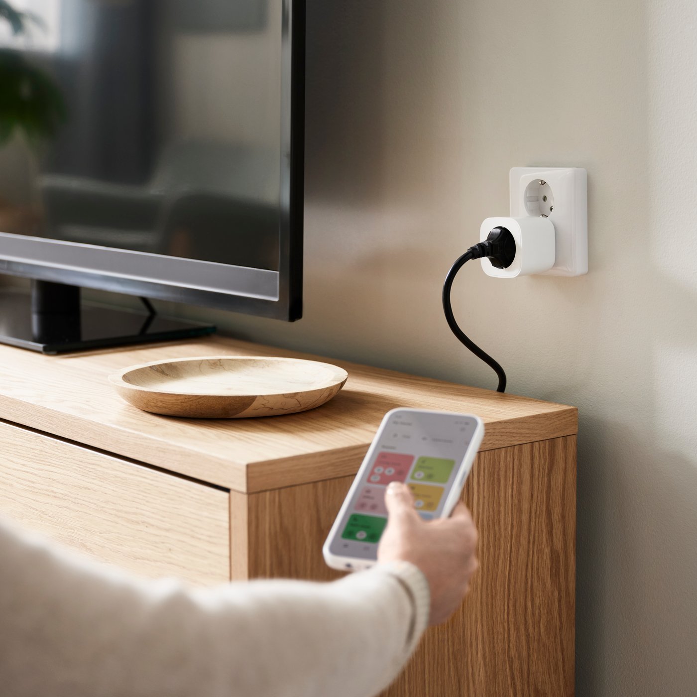 Bela utičnica na zidu, muškarac koji drži IKEA Home smart daljinski upravljač ispred utičnice.