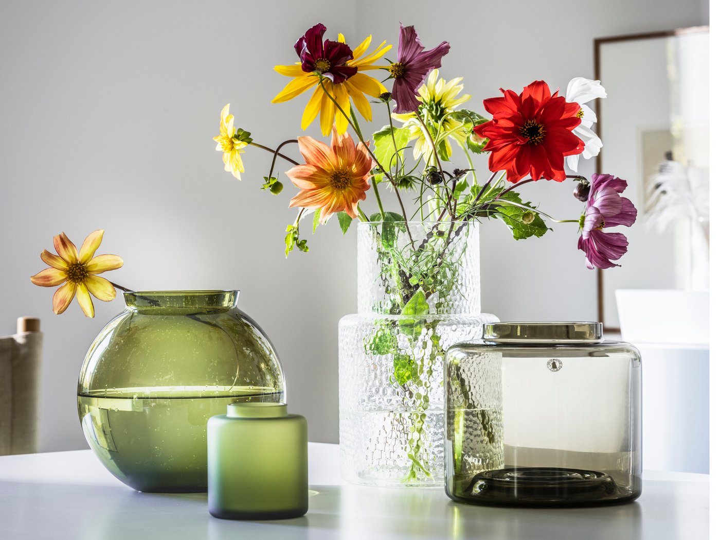 Auf einem weißen Tisch stehen verschiedene Vasen in grün und weiß. Darin sind bunte Blumen