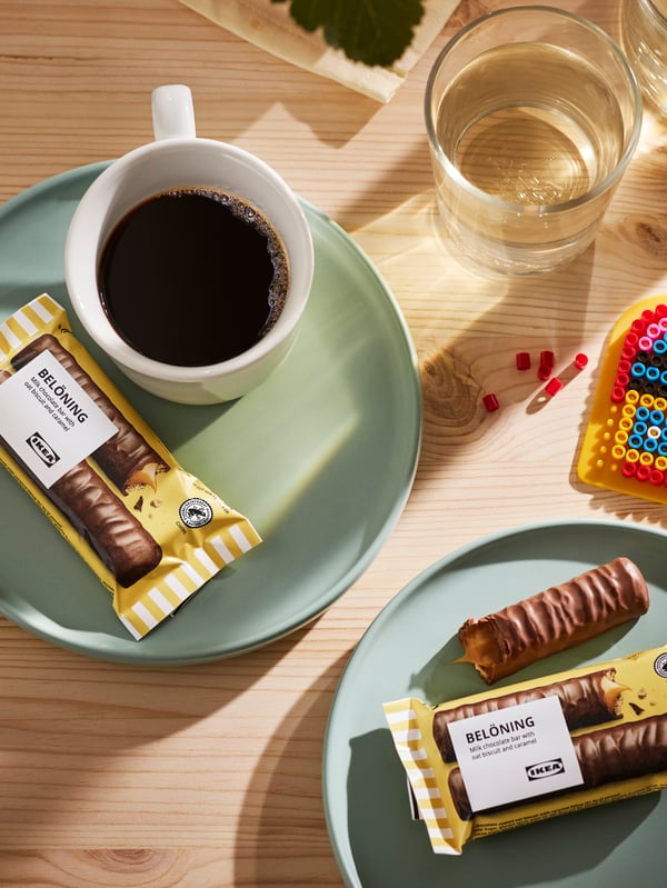 Green plates holding BELÖNING milk chocolate bars with oats and caramel, one of the plates has a white coffee cup on it.