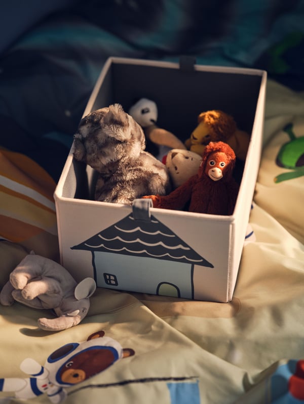 Bež BARNDROM kutija u kojoj se nalaze plišane igračke uključujući LILLEPLUTT mačku i DJUNGELSKOG orangutana na vrhu kreveta.