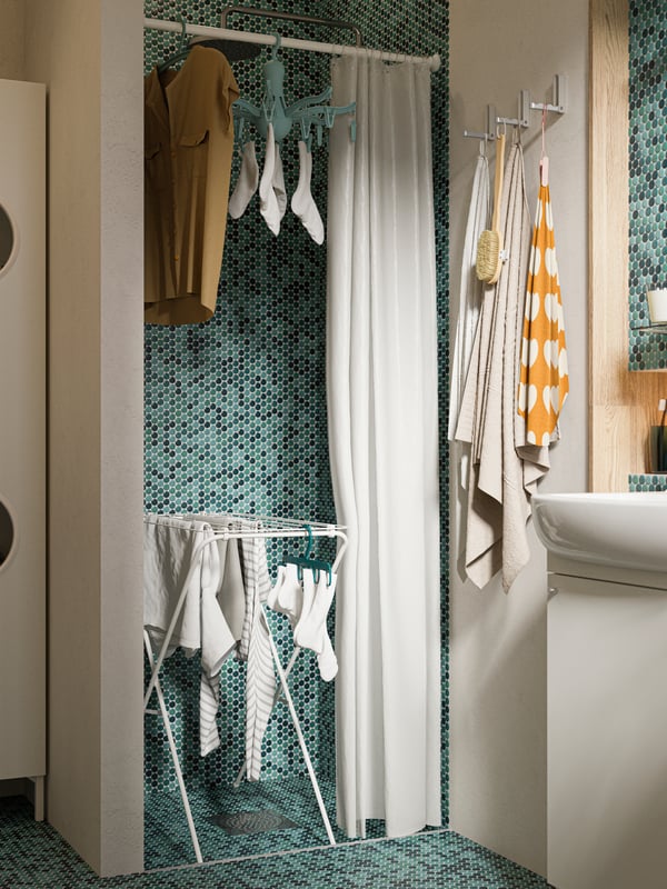 Vista de habitación de baño con una pared escondida con una cortina utilizada para secar la ropa. Con un colgador PRESSA y un tendedero JÄLL.