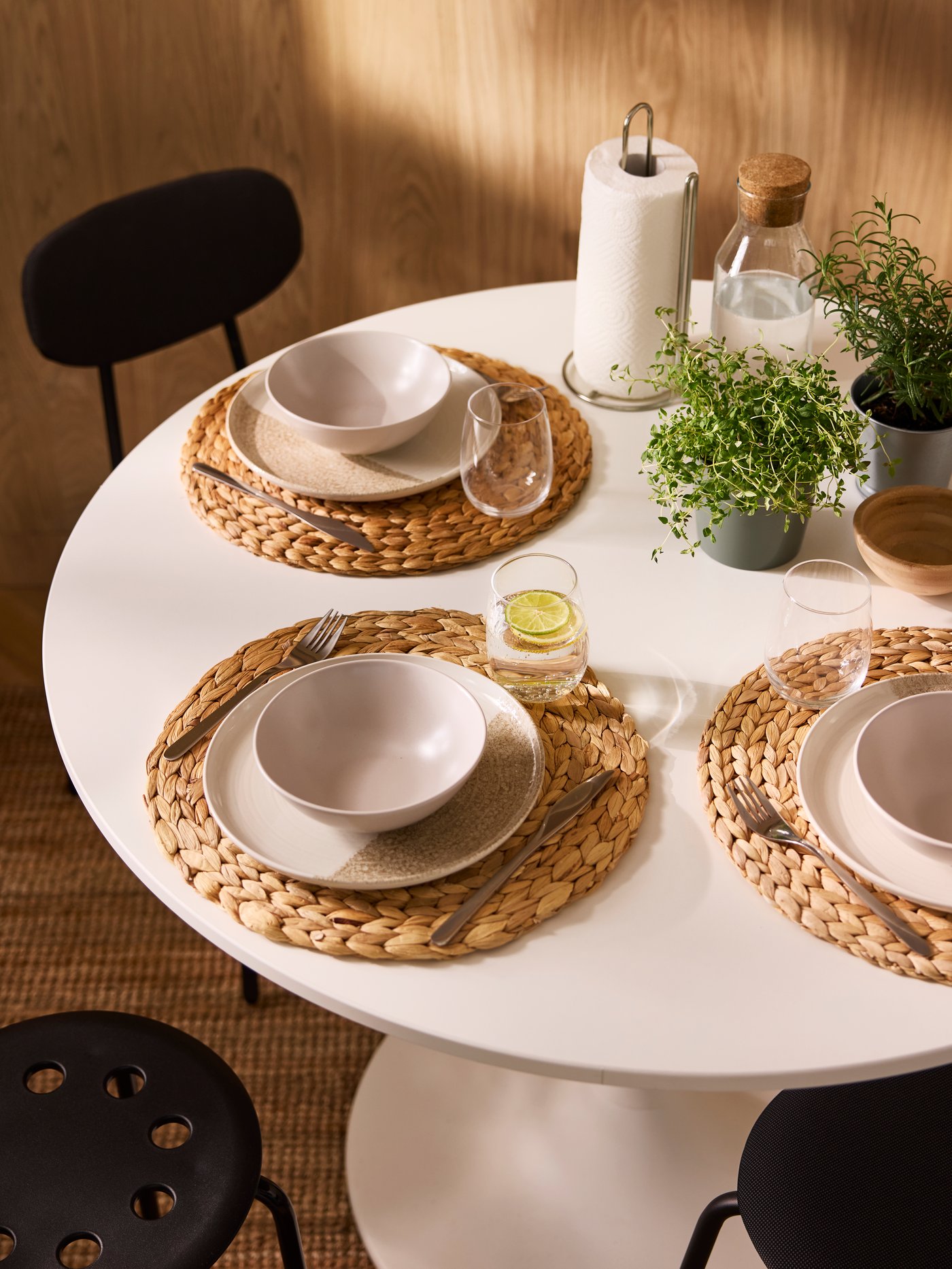 A sun-dappled dining area with a white, round DOCKSTA table set with potted herbs and tableware on round SOARÉ place mats.