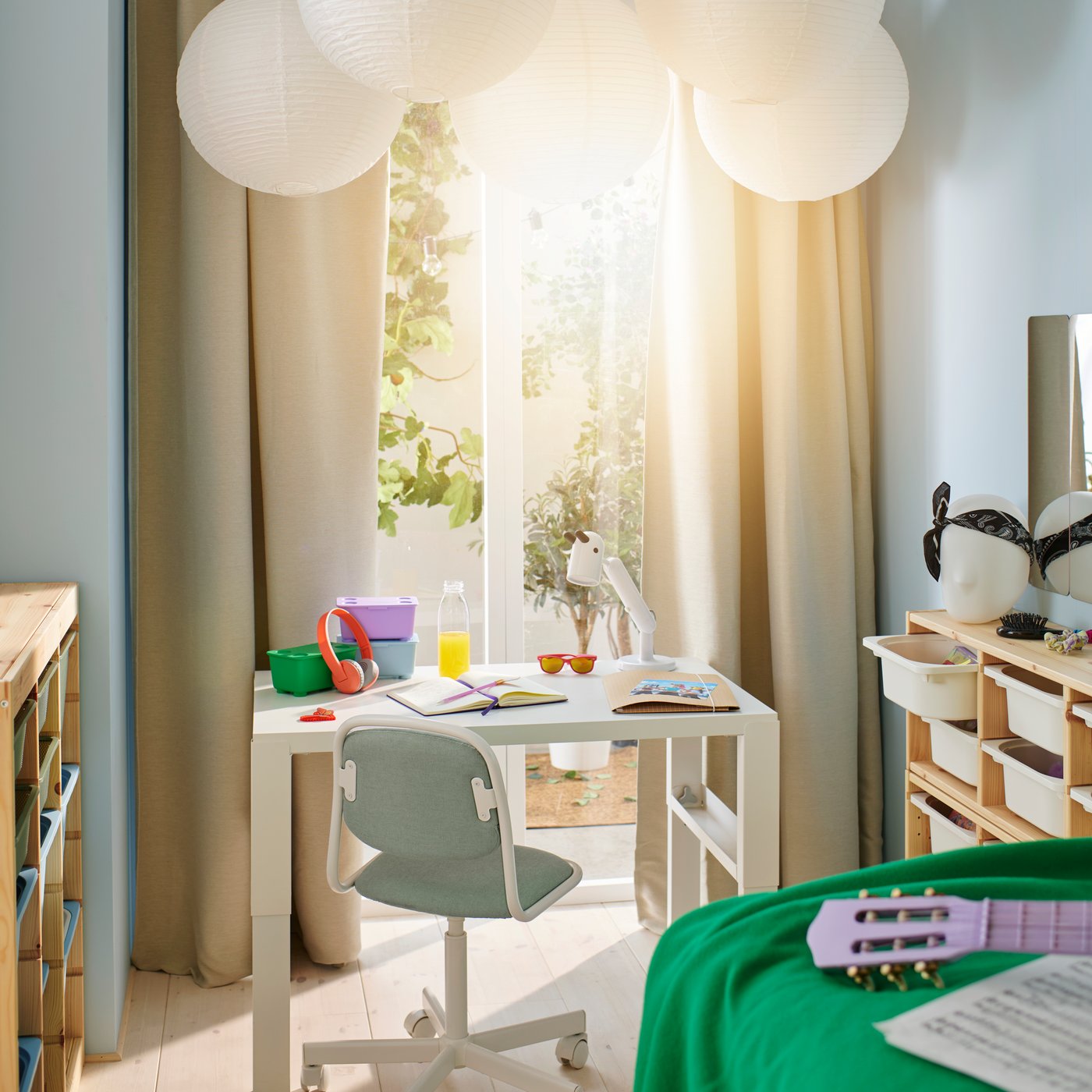 Ein weißer PÅHL-Schreibtisch in einem hellen, sonnigen Raum, auf dem grüne, lila und blaue GLIS-Boxen stehen und eine weiße KRUX-LED-Arbeitsleuchte angebracht ist.