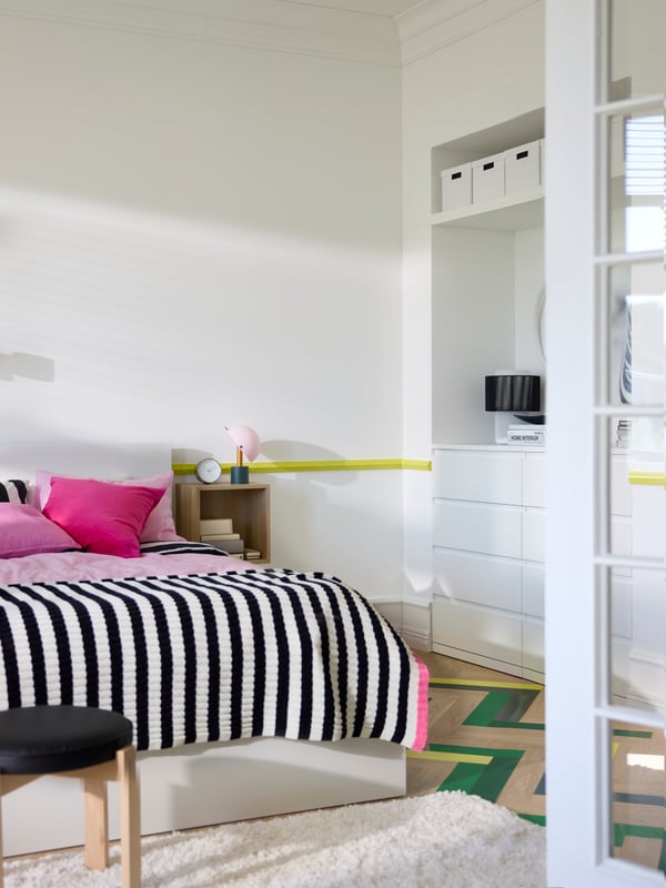 View of bedroom through open glass doors, with crisp white walls and storage combinations, double bed in middle.