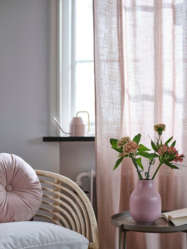 En GRADVIS vas står på ett sidobord framför ett fönster med ljusrosa SILVERLÖNN gardiner.