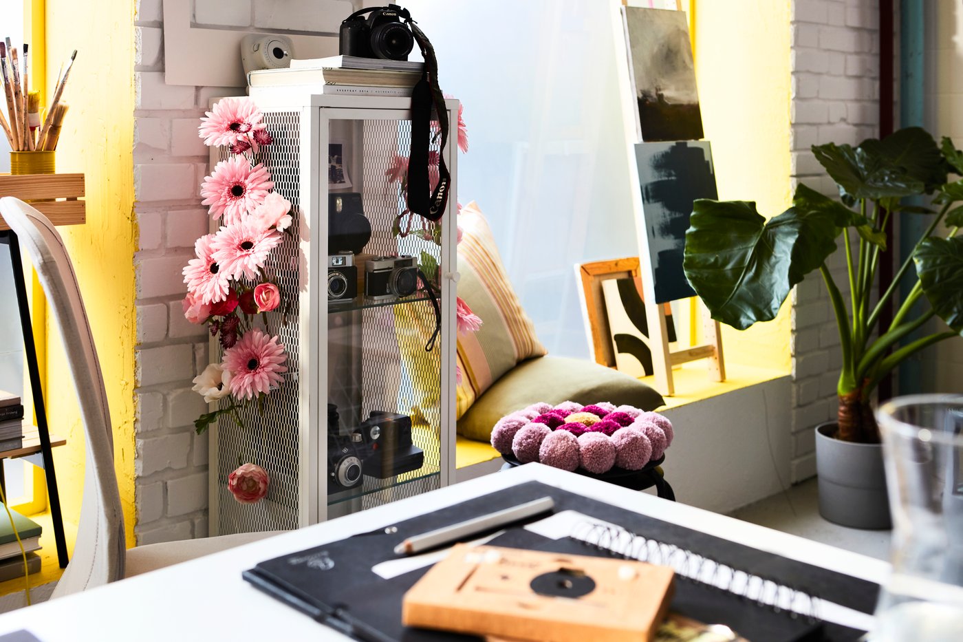 Es ist ein farbenfrohes Büro mit einer BAGGEBO Vitrine zu sehen, die mit künstlichen SMYCKA Blumen geschmückt ist.
