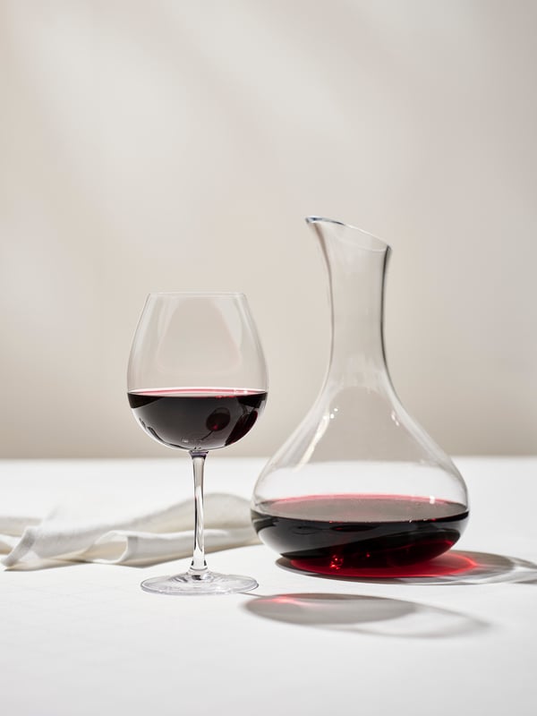 Do pola puna STORSINT čaša za crno vino, pored bele platnene salvete i STORSINT prozirnog staklenog karafa u kome se nalazi crno vino.