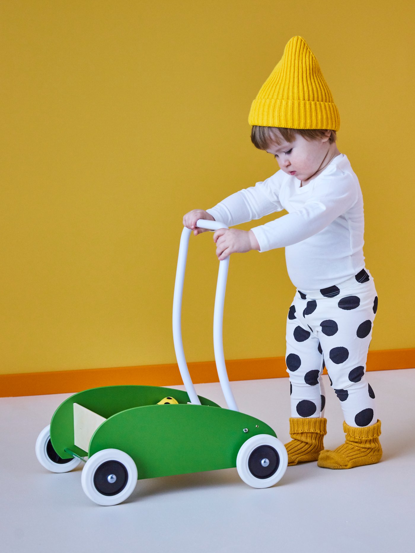 Un bébé pousse un chariot de marche vert en tenant la poignée blanche.