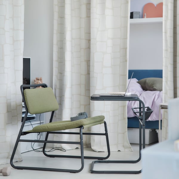 An olive-green LINNEBÄCK easy chair in an airy and white small living room with a textile room divider and a black table.