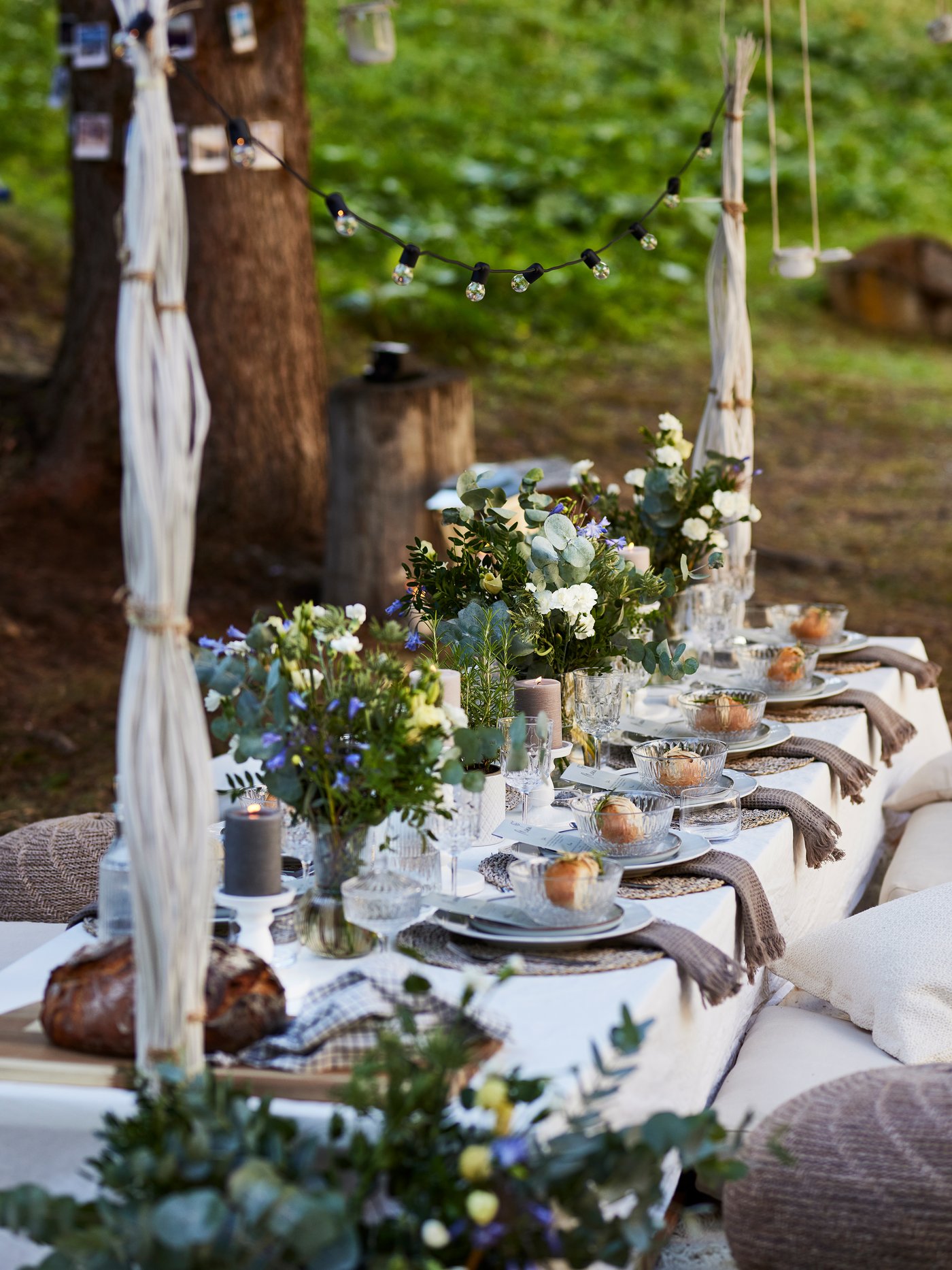 A low wedding table covered with flowers and dishes, around which are various seat cushions. Everything is decorated with flowers and fairy lights. 