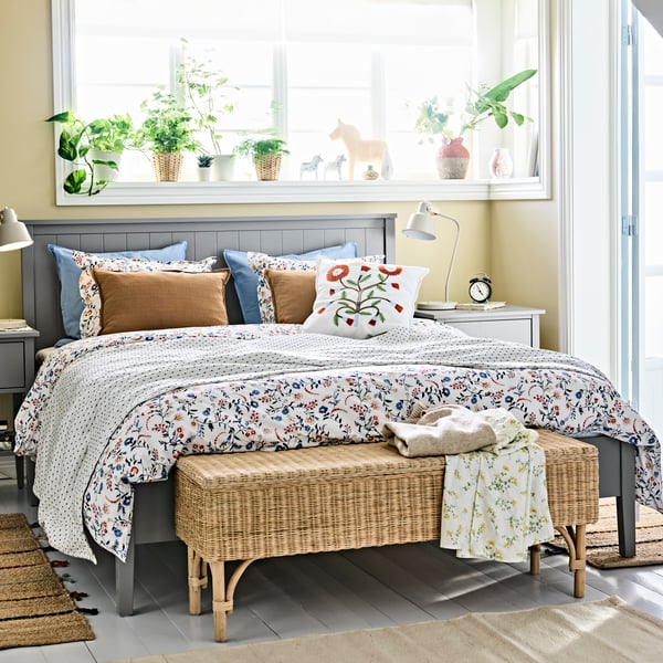 A bedroom setup featuring a neatly made bed with patterned textiles, bedside tables on each side and a woven bench in front.