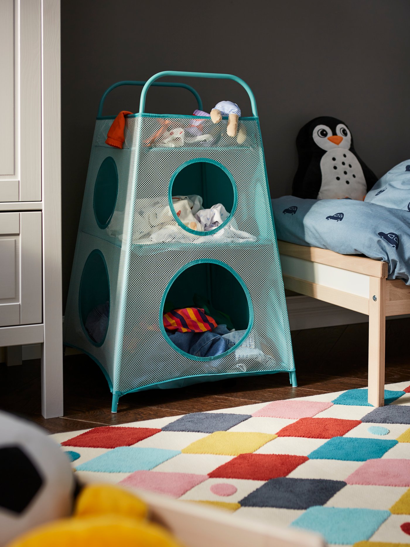A childs room setting with a blue storage unit. A diamond multi-color rug sits on the floor.