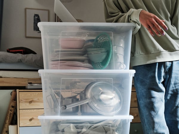 Una persona sostiene cajas plásticas con utensilios de cocina dentro de una caja plástica.