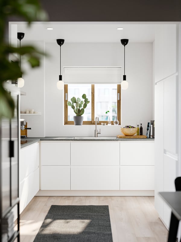 A small kitchen with white walls and smooth white VOXTORP fronts has three black pendant lamps and a gray rug on the floor.