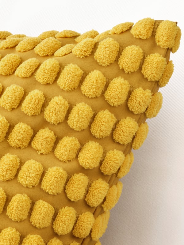 A close-up of a corner of a cushion covered in a yellow SVARTPOPPEL cushion cover.