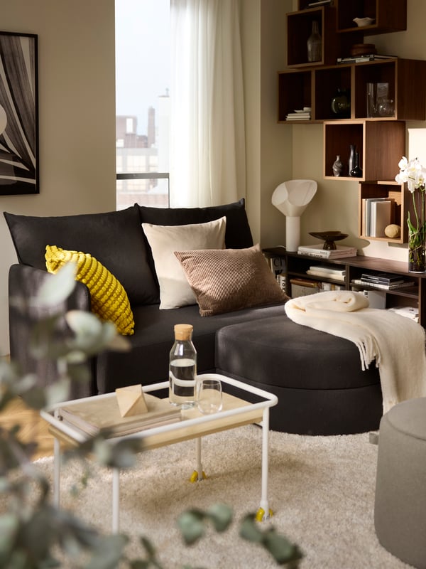 Helles Wohnzimmer mit einem dunkelgrauen LINDÅKRA Bettsofa, EKET Schränken, Textilien, Deko und einem VOLLERSLEV Teppich.