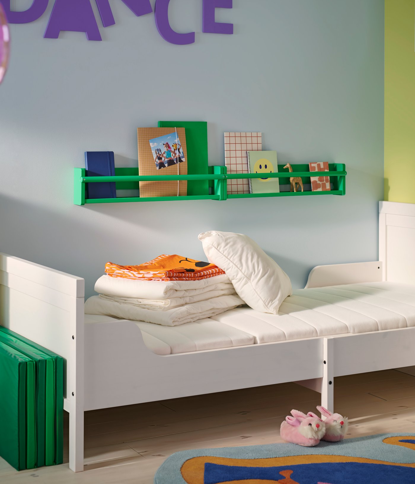 A white BUSUNGE extendable bed with a VIMSIG foam extendable mattress in a blue children’s room with folded textiles on top.