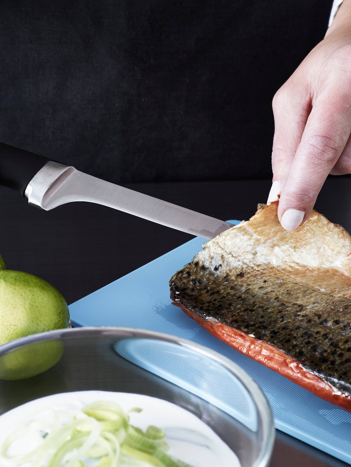 A person wearing a black apron is filleting a piece of fish using a fillet knife with a black handle.