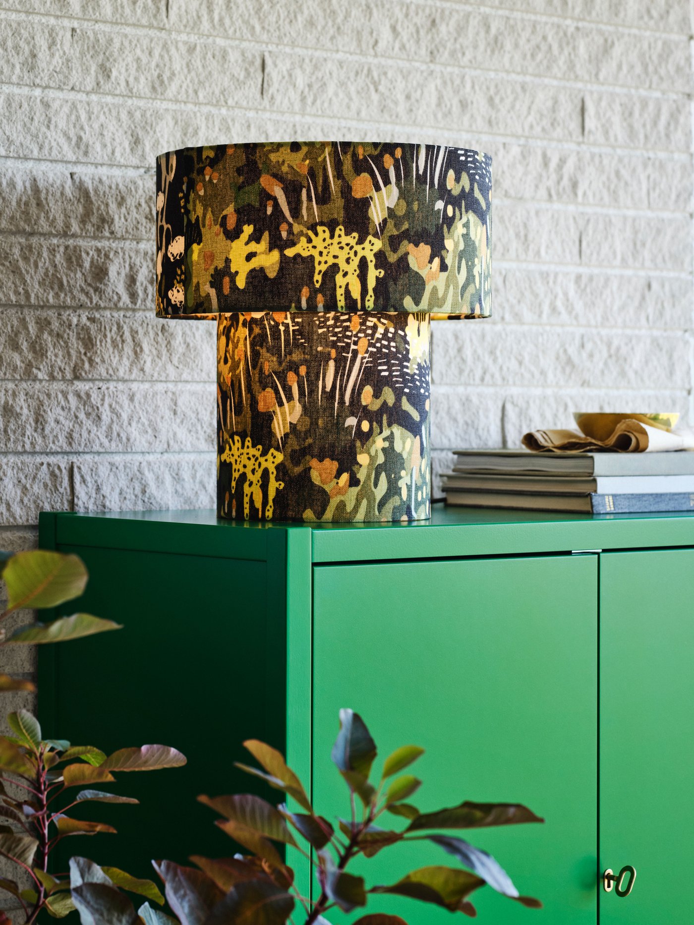 Un gabinete verde con una lámpra de mesa con decoración de plantas encendida.