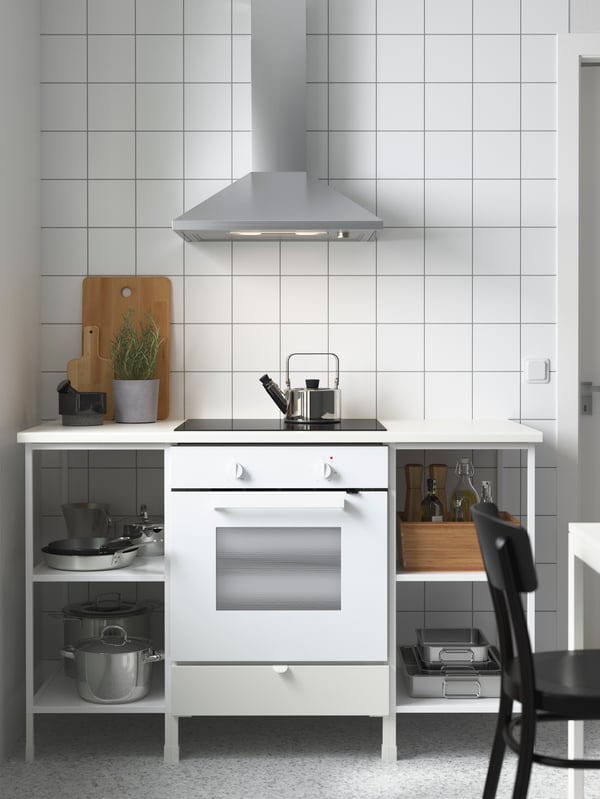 A white ENHET kitchen with pots, pans and oven trays on the shelves. An extractor hood in stainless-steel hangs above.