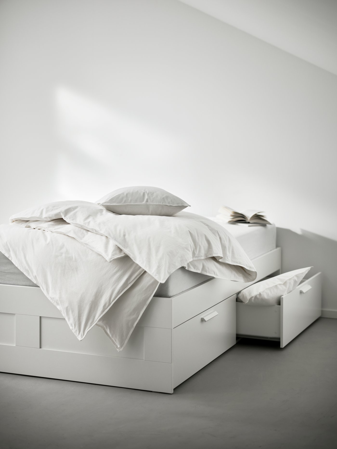 Una cama doble con almacenamiento son plumones y almohadas sobre el colchón.