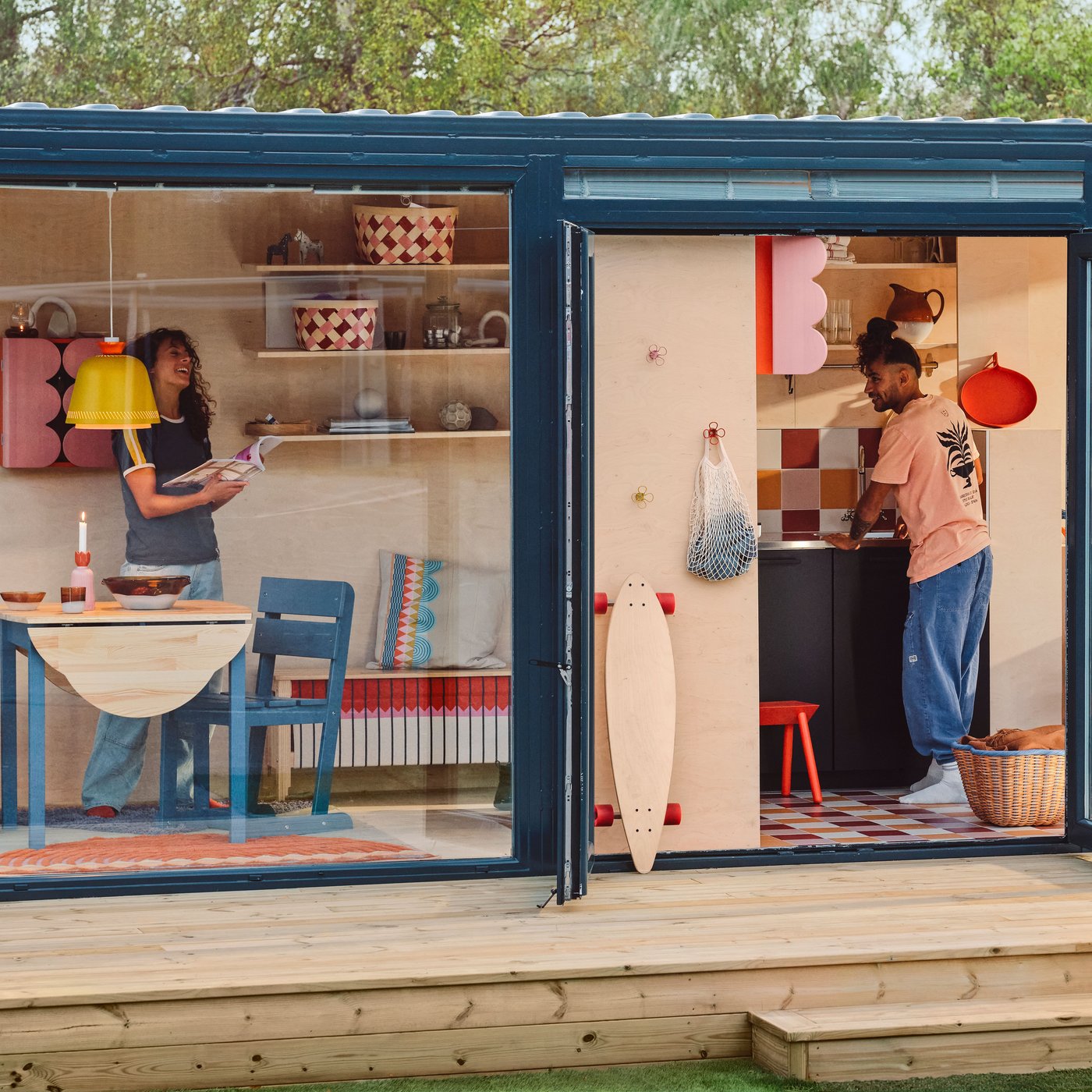 A tiny house on a deck, with glass walls and doors, seen from outside. There are OMMJÄNGE furnishings and decorations inside.