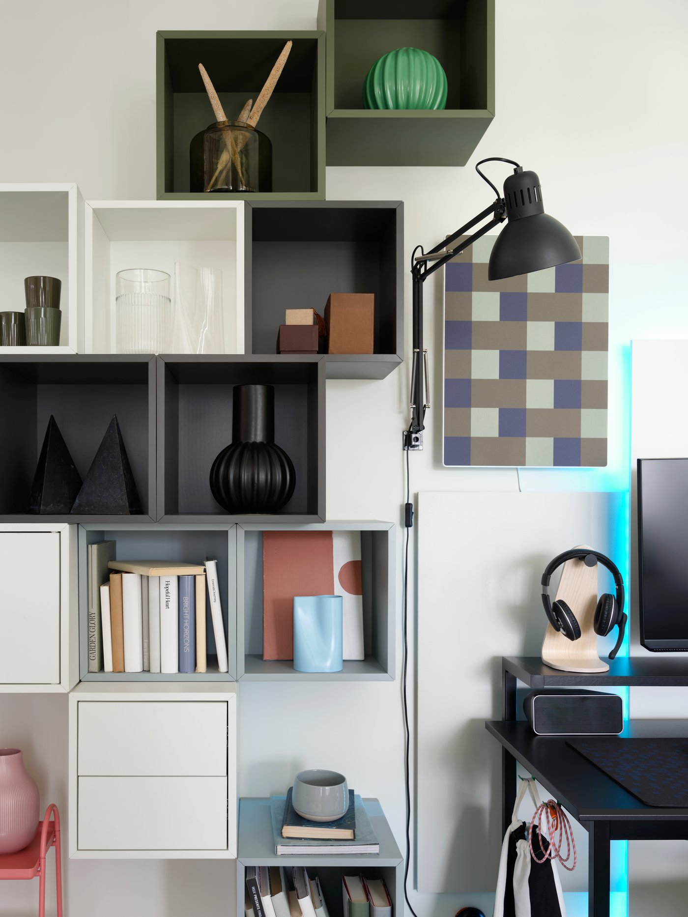 Beside a desk is an asymmetrical grouping of various EKET wall-mounted shelving units that hold modern decor and books.